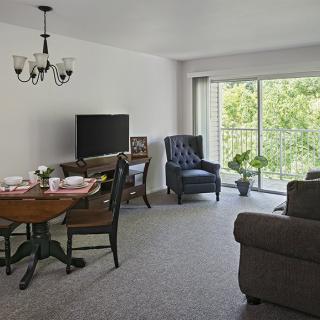 A cozy living room with a dining area, featuring a television, sofa, and large window overlooking greenery.
