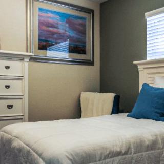 A cozy bedroom with a single bed, dresser, and a framed painting on the wall.
