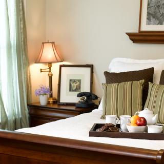 A cozy bedroom with a neatly made bed, featuring decorative pillows and a tray with tea and fruit.