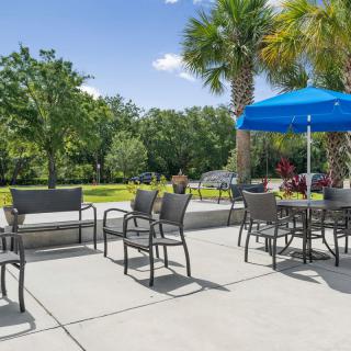 A sunny outdoor patio area featuring tables and chairs surrounded by lush greenery.