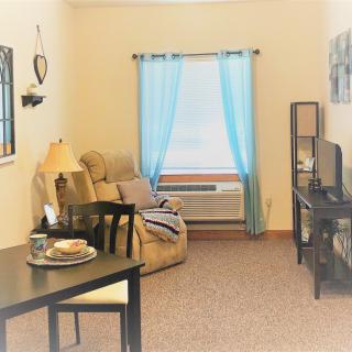 A cozy living room with natural light, featuring a comfortable chair, TV, and a small dining table.