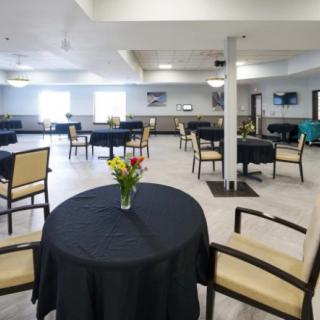 A spacious dining area with tables covered in black tablecloths, adorned with a vase of flowers.