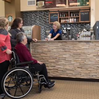 A group of customers interacting with a staff member at a caf, with one person in a wheelchair.