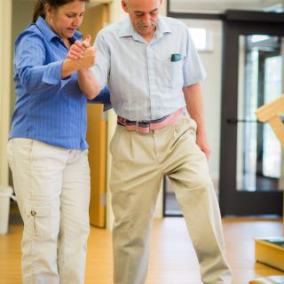 A therapist assists an elderly man with physical rehabilitation exercises.