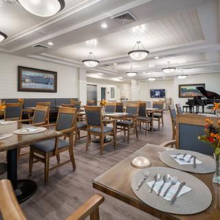 A modern and elegantly designed restaurant dining area with neatly arranged tables and chairs, featuring chandelier lighting and a grand piano.