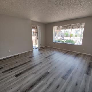 A spacious living room with hardwood flooring and a large window allowing natural light to fill the space.