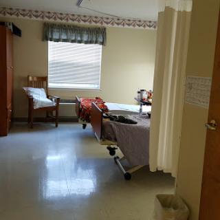 A view of a hospital patient room featuring a bed, seating area, and natural light from the window.