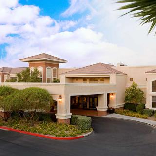 A modern hotel building with a landscaped entrance and a blue sky backdrop.