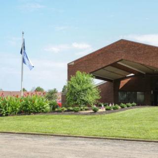 A modern brick building with a landscaped lawn and flags flying nearby under a clear blue sky.