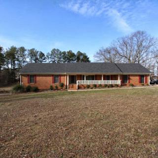 A spacious single-story brick house surrounded by a well-maintained landscape and clear blue skies.