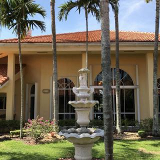 A charming outdoor scene featuring a decorative fountain surrounded by palm trees and a building with arched windows.