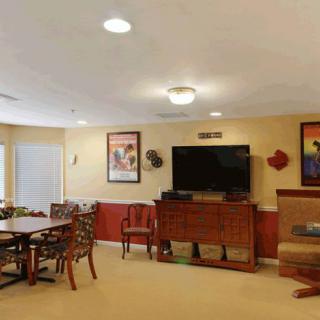 A cozy living room with a television, chairs, and a table, adorned with wall decorations.