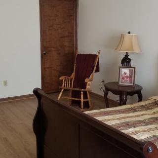 A cozy bedroom corner with a wooden rocking chair, side table, and lamp.