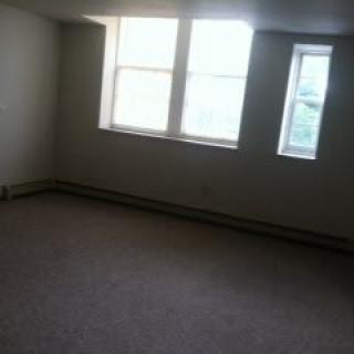 An empty room with carpet flooring and large windows letting in natural light.