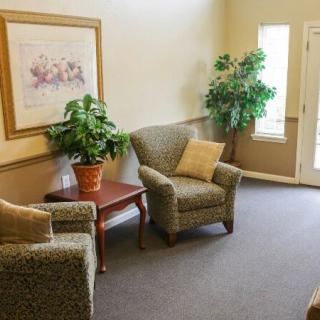 A cozy waiting room with two armchairs, a small table, artwork on the wall, and potted plants.