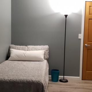 A minimalist bedroom with a single bed and a floor lamp against gray walls.