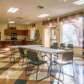 A well-lit multipurpose room with a decorated tree, featuring a table and chairs, and a kitchen area.
