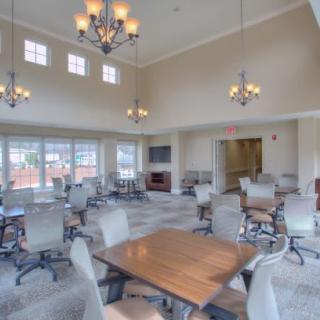 A spacious dining area with multiple tables and chairs, illuminated by chandeliers, featuring large windows and a neutral color scheme.