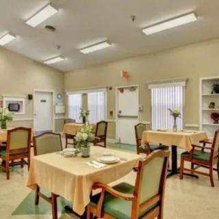 A well-lit dining area with tables and chairs arranged neatly, featuring simple decor and large windows.