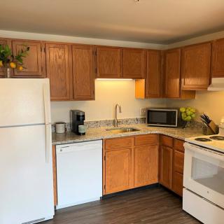 A cozy kitchen featuring wooden cabinets, a white refrigerator, dishwasher, microwave, and a coffee maker.