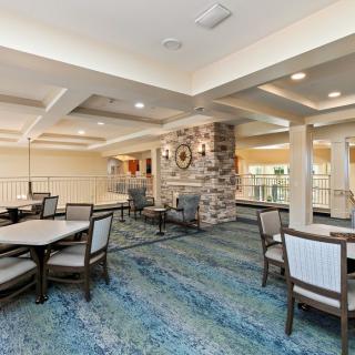 A spacious and well-lit dining area with neatly arranged tables and chairs, featuring a stone wall accent and blue carpeting.