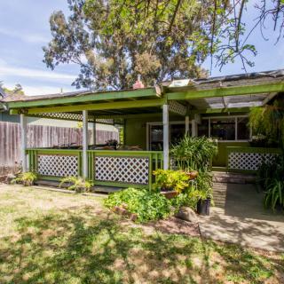 A charming backyard view of a house with a covered patio surrounded by greenery.