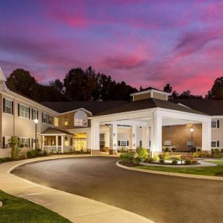 A beautifully lit building exterior at sunset with a curved driveway and landscaped surroundings.