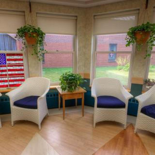 A cozy waiting room with wicker chairs and decorative plants, featuring a piece of American flag artwork by the window.