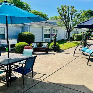 Sunny patio area with tables, chairs, and umbrellas surrounded by greenery.