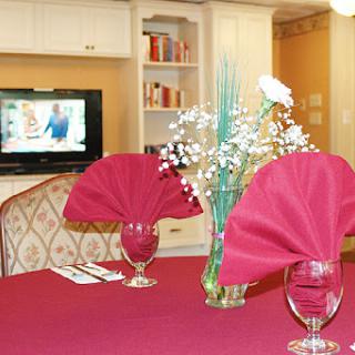 A beautifully set dining table with red napkins and decorative flowers, complemented by a television in the background.