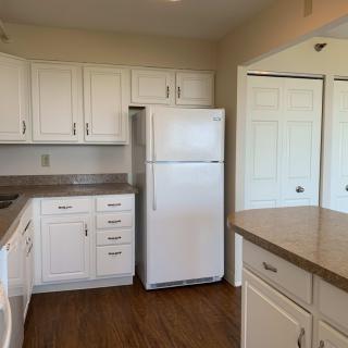 A kitchen with white cabinets, a refrigerator, and wooden flooring.