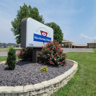 Welcome sign for a local business, surrounded by neatly landscaped flowers and greenery.