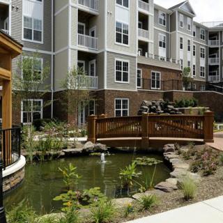 A modern apartment complex with a landscaped pond and wooden bridge in the courtyard.