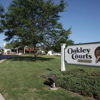 Entrance sign for Oakley Courts with lush greenery and buildings in the background.