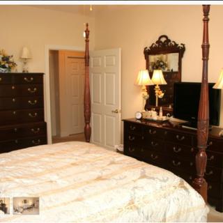A cozy bedroom featuring a four-poster bed, dresser with mirror, and bedside lamps.
