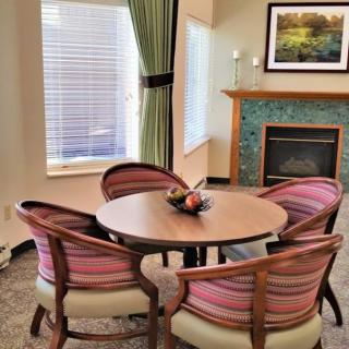 A cozy dining area with a round table and chairs, set near a fireplace in a well-lit room.