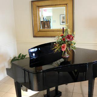 A grand piano adorned with a floral arrangement, positioned in front of a wall mirror.