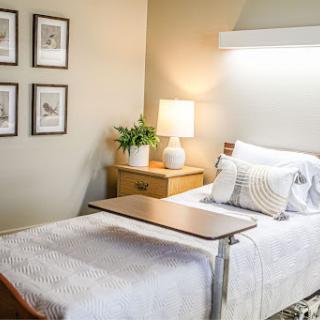 A serene hospital room featuring a neatly made bed, bedside lamp, and decorative artwork on the wall.