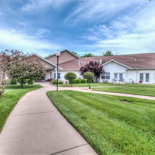 A well-maintained lawn and sidewalk lead to a residential house under a partly cloudy sky.