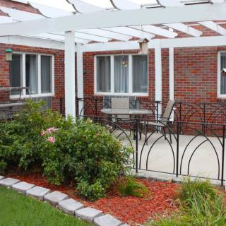 A cozy outdoor patio with a white pergola, surrounded by a well-maintained garden and brick walls.