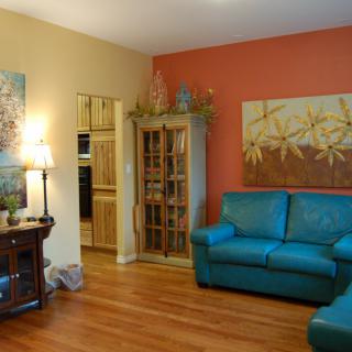 A modern living room featuring a turquoise sofa, wooden flooring, and contemporary artwork.