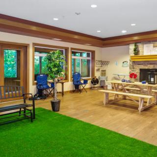 A cozy indoor room with a mix of natural and rustic elements, featuring a fireplace, wooden furniture, and artificial grass flooring.