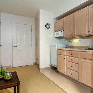 A compact apartment kitchen with light wooden cabinets and a microwave above the countertop.