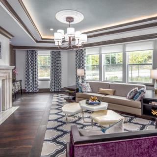 A modern living room with elegant decor, featuring a large sofa, geometric carpet, and a central chandelier.