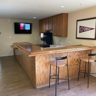 A cozy home bar area with a wooden counter, stools, and a television.