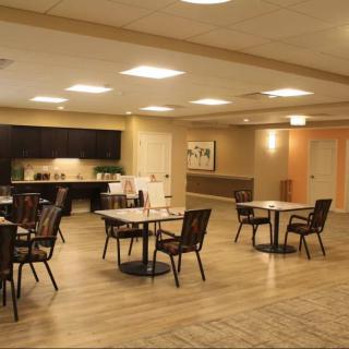 A spacious dining area with tables and chairs, featuring a kitchenette in the background.