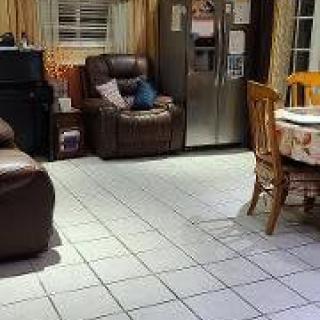 A cozy kitchen and living area with tiled floors, including a dining table, refrigerator, and sofa.
