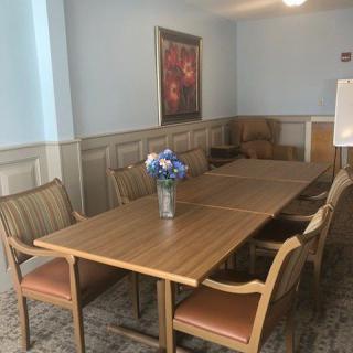 A meeting room with a wooden conference table, surrounded by chairs and decorated with a flower vase and painting.