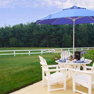 A tranquil patio setup with a table, chairs, and an umbrella overlooking a lush green lawn and white fence.