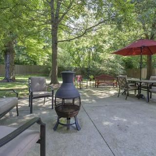 A tranquil patio setting with a chiminea, surrounded by outdoor furniture and shaded by trees.